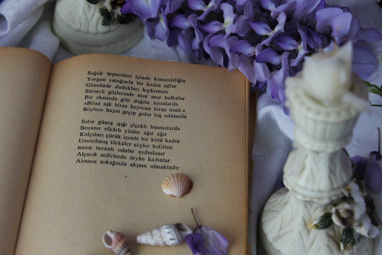 An open vintage book with poetry surrounded by purple flowers and seashells.